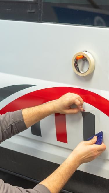 Person applying a red and black decal to a vehicle