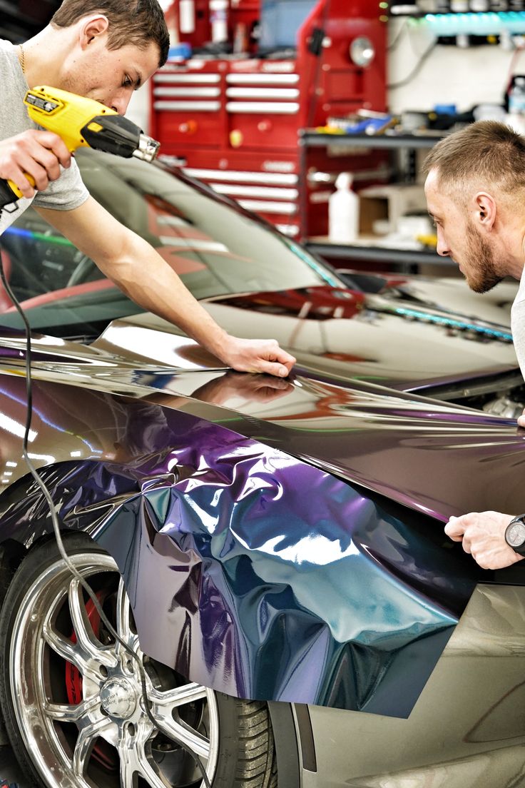 Two men working on a car with a reflective wrap in a garage setting.