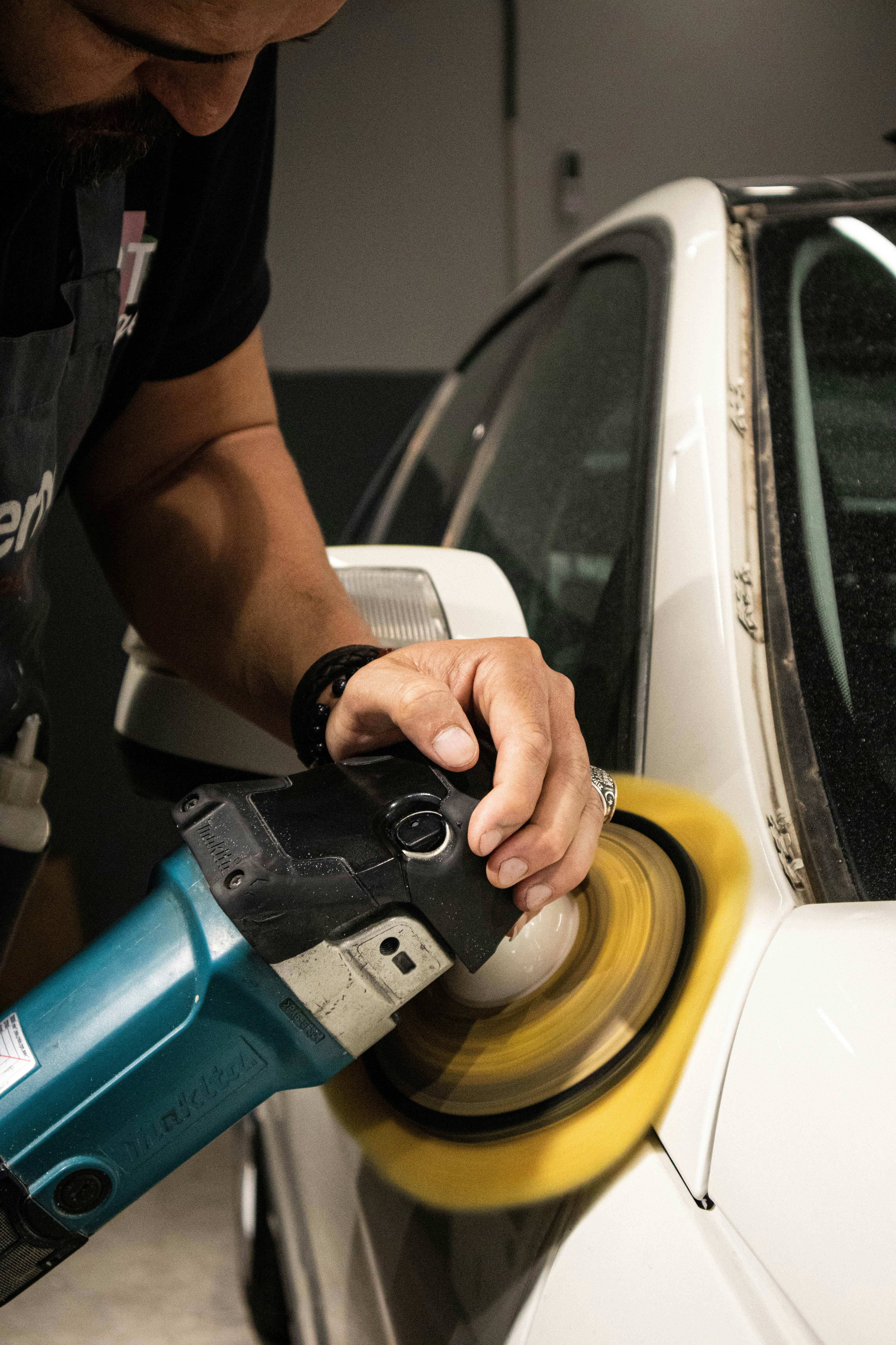 Person using a car polisher on a white car in a garage.