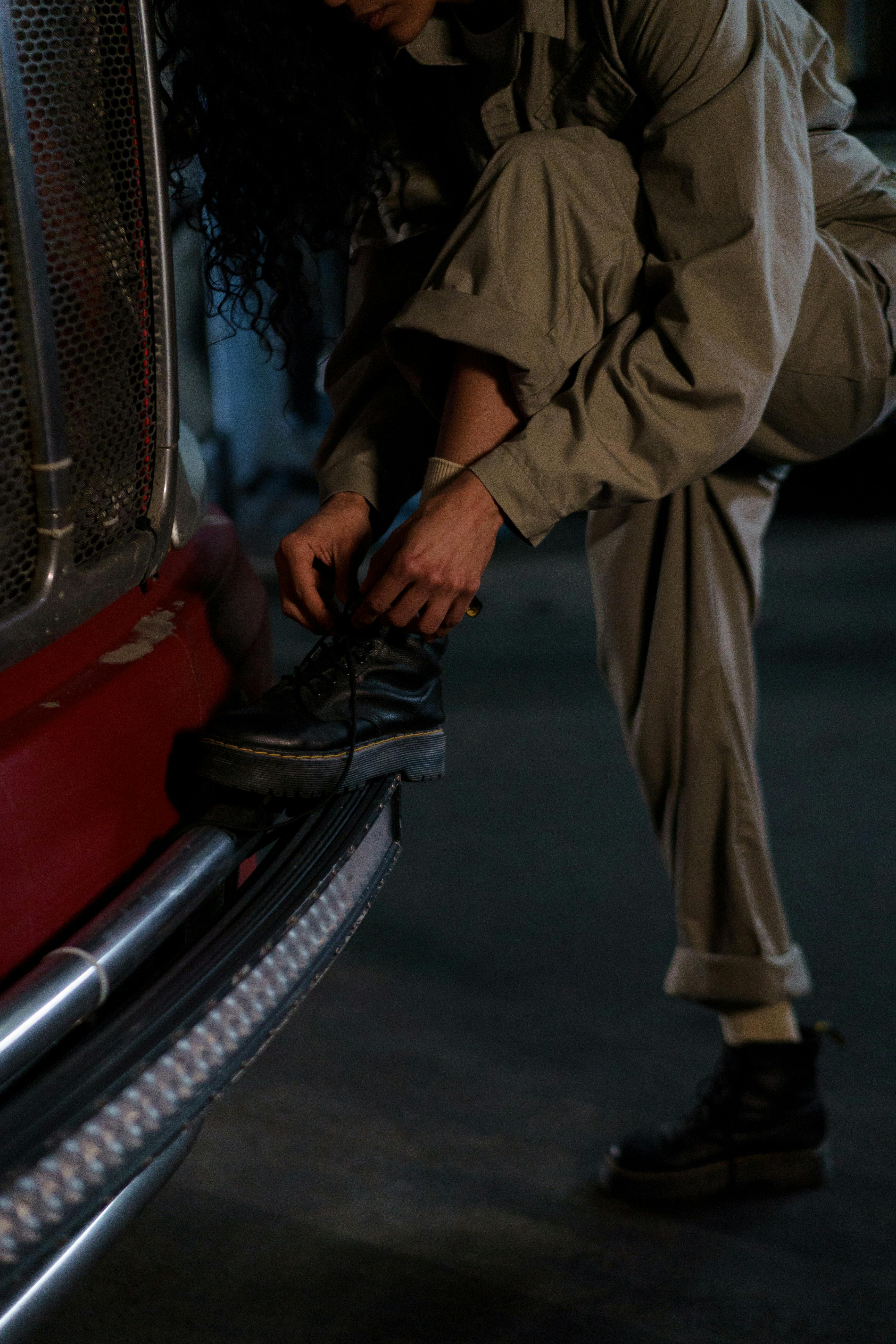Person adjusting a boot near a red vehicle in a dimly lit setting