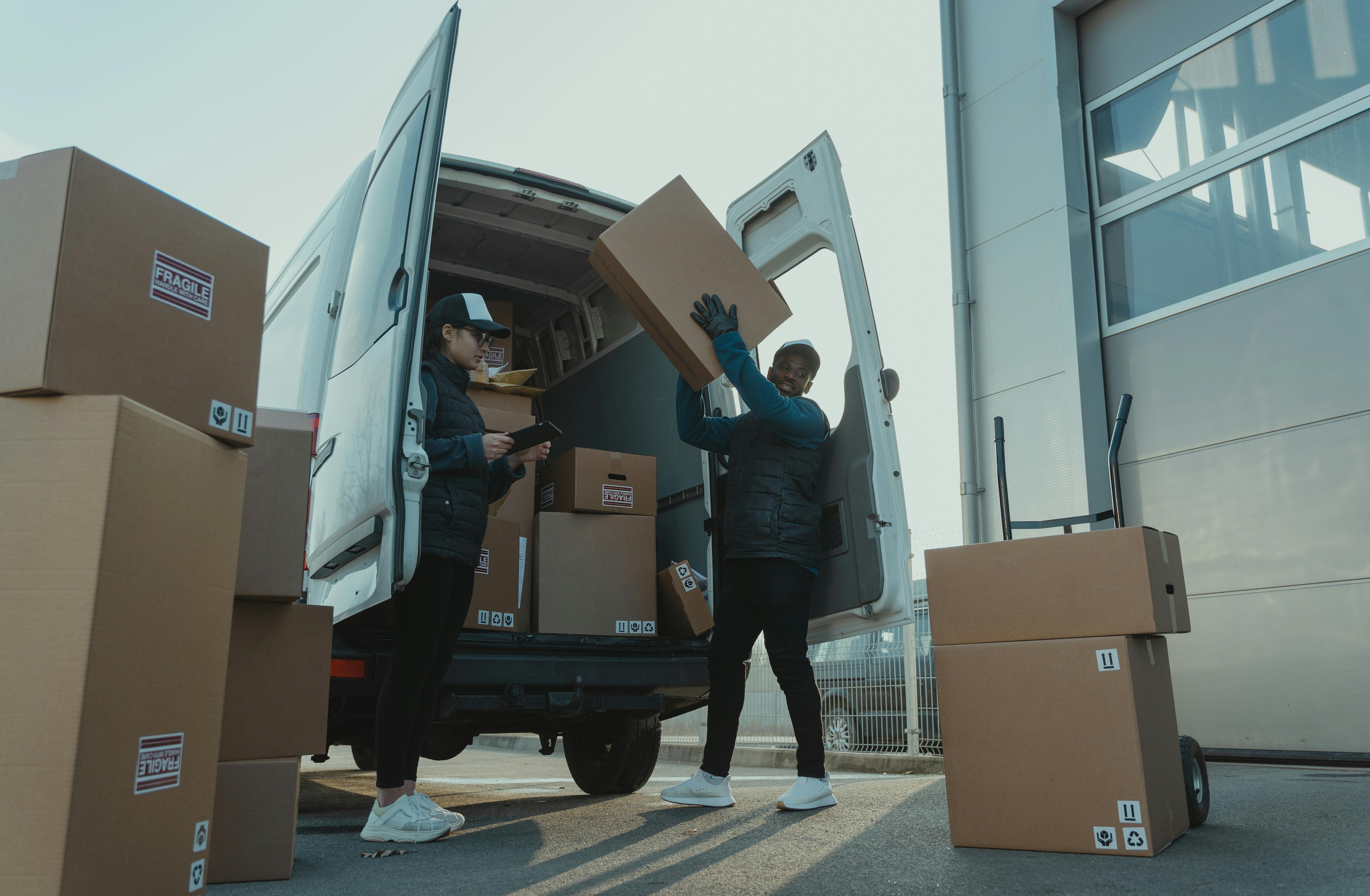Two people unloading boxes from a van outside a building.