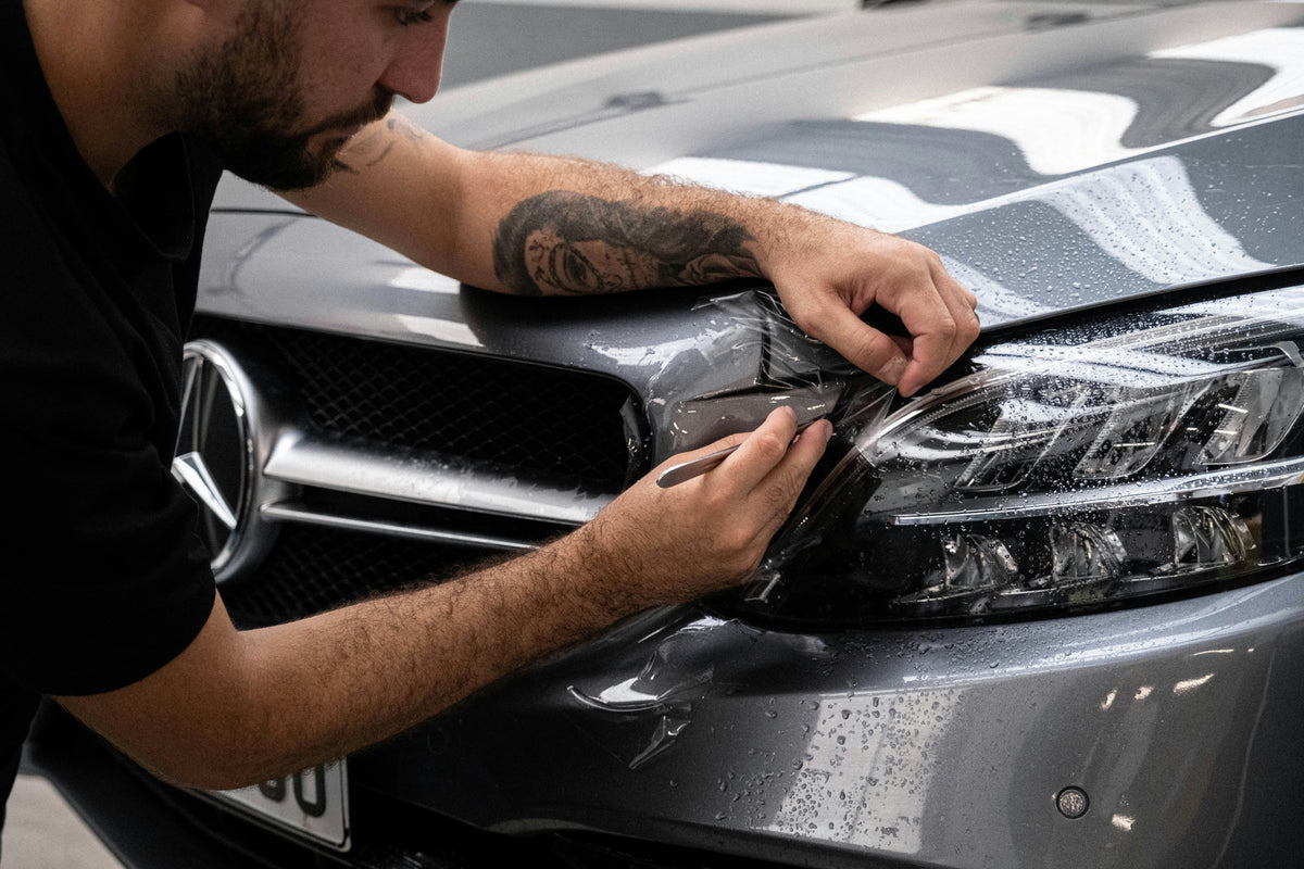 Technician aligning PPF on vehicle headlights for precise fit.