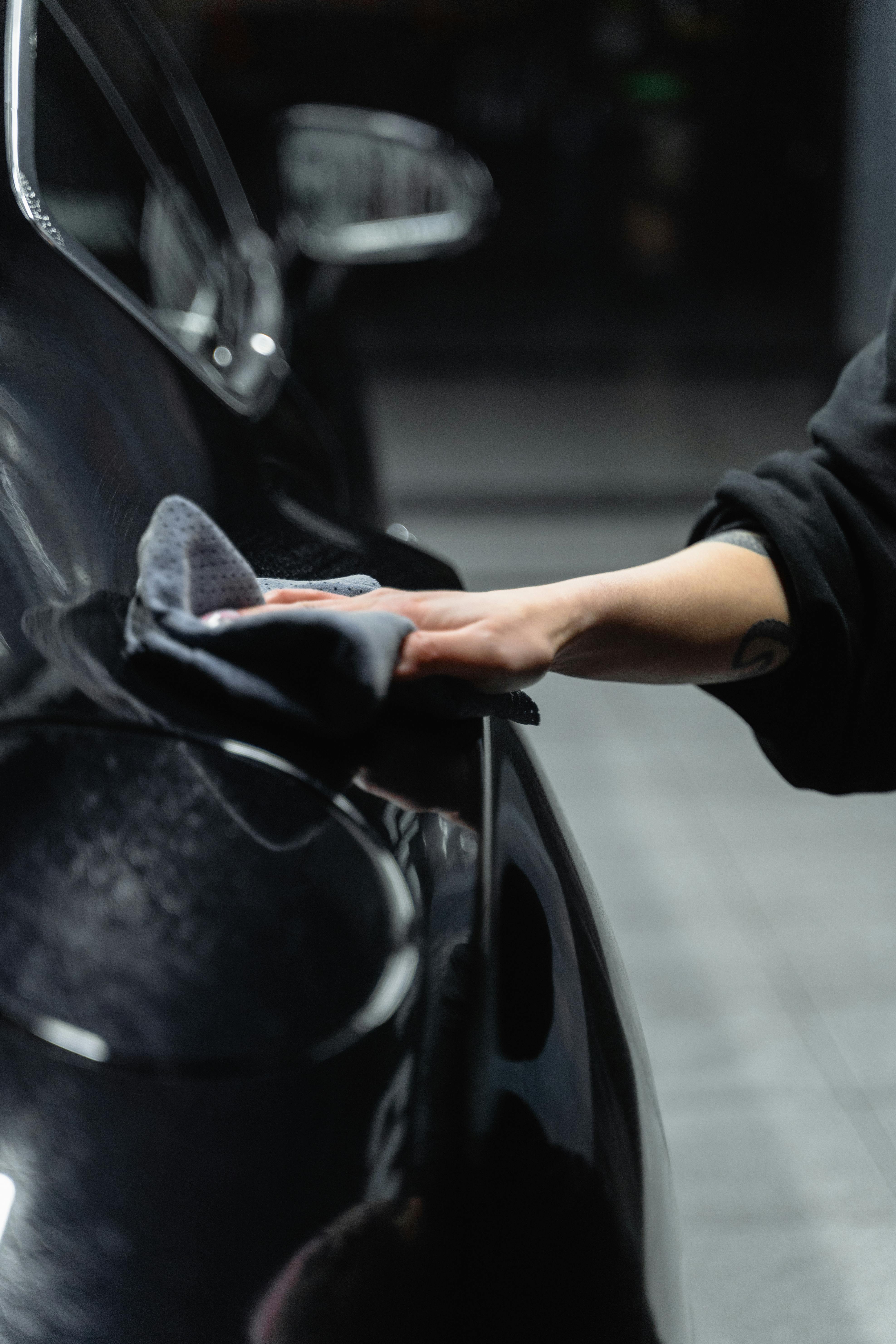 Detailer cleaning and polishing a car interior dashboard using microfiber cloths and detailing spray.