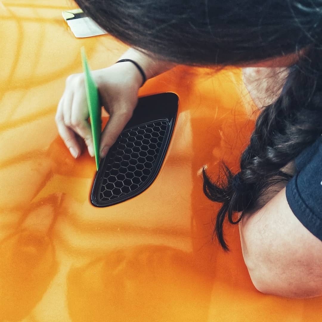A professional applying a vibrant vinyl car wrap to a vehicle hood using a squeegee tool.