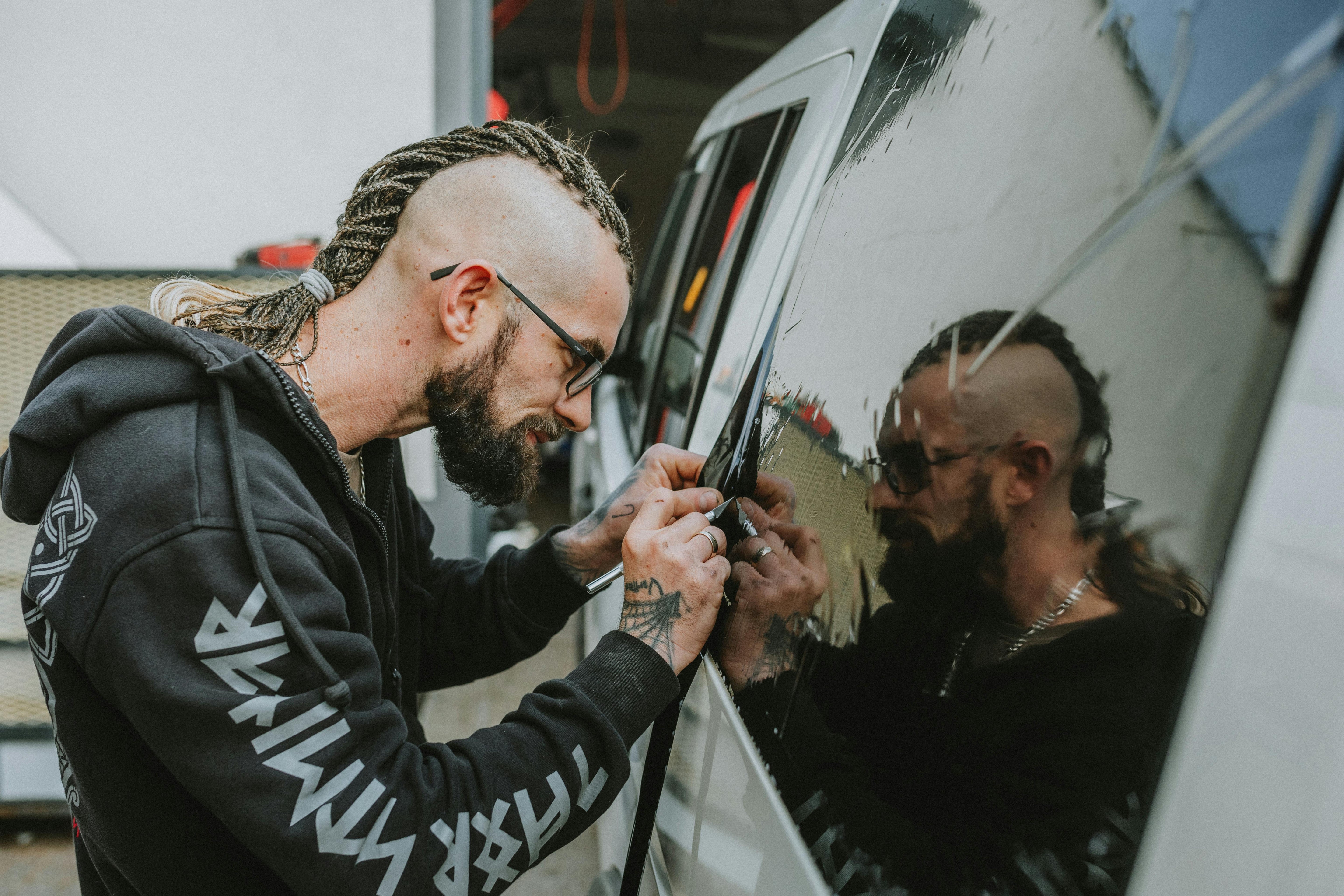 Male installer smoothing automotive window tint with a squeegee tool.