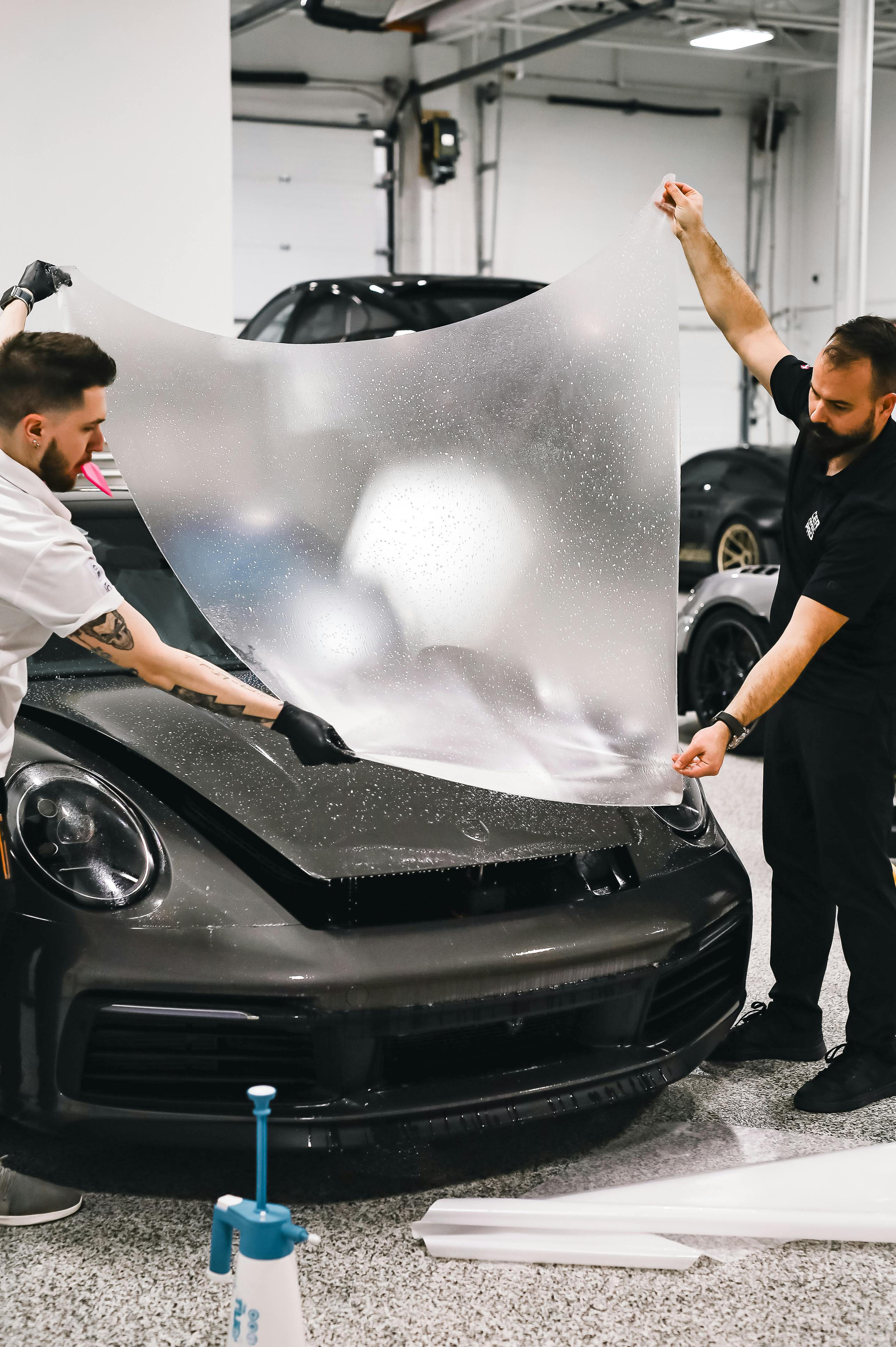 Professional applying paint protection film to front bumper area.