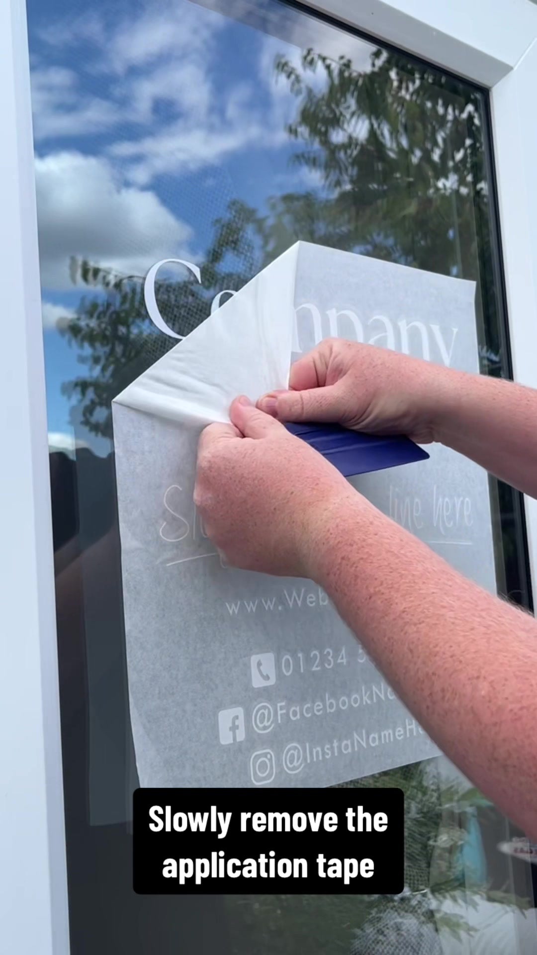 Worker in high-visibility vest installing large adhesive signage on a shopfront window using application tools.