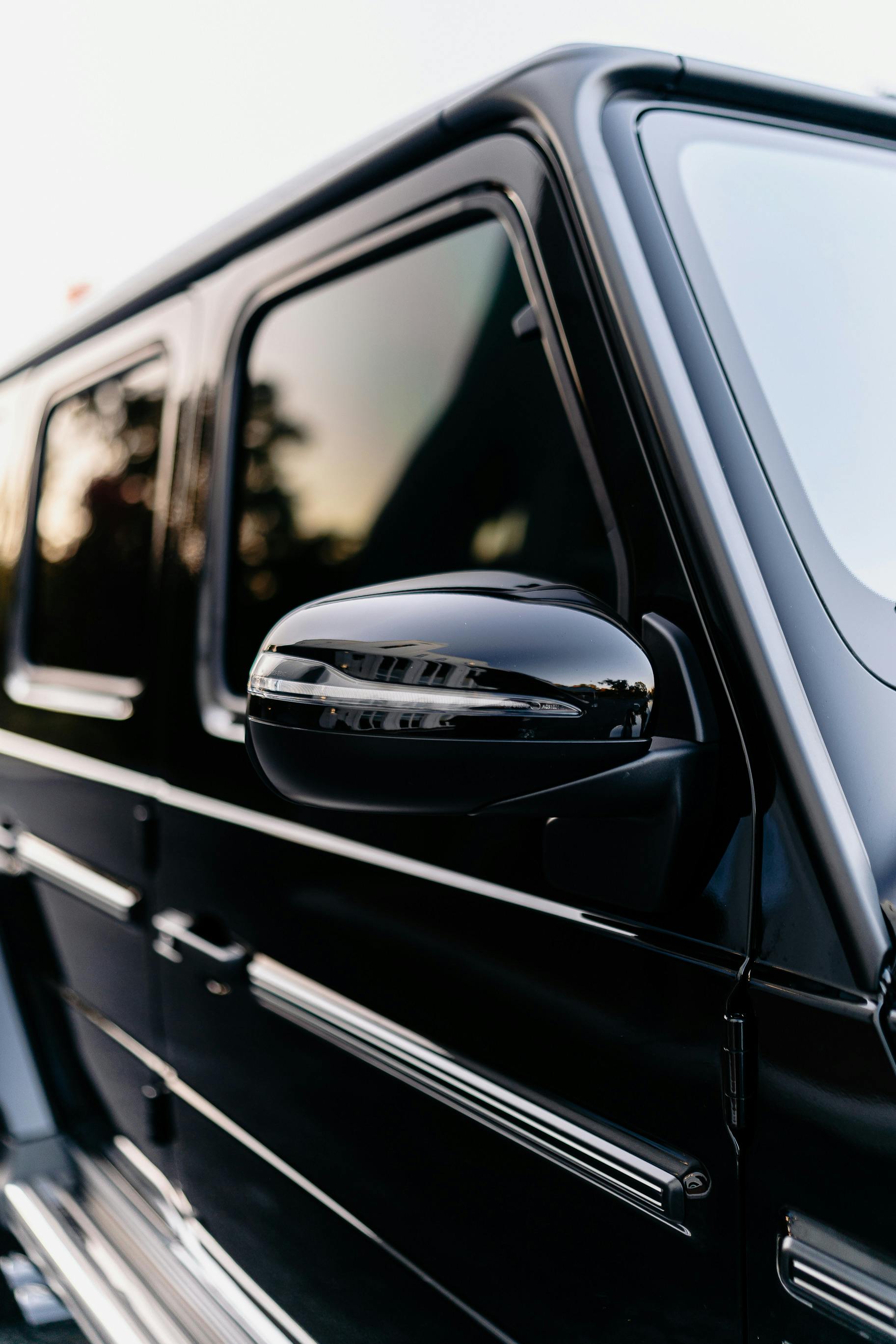 Installer smoothing dark window tint film onto a car side window with a heat gun and squeegee.